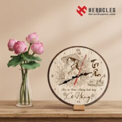 Đồng hồ gỗ để bàn hình tròn khắc laser hình cô giáo mặc áo dài nón lá và chữ Tri Ân 20/11, quà tặng từ học trò Cẩm Nhung kính tặng cô Hằng, đặt cạnh bình hoa sen hồng trên mặt bàn gỗ.