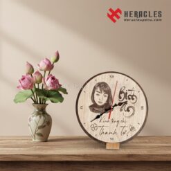 Đồng hồ gỗ tròn để bàn in hình chân dung vẽ chì và khắc tên cá nhân, quà tặng tri ân tinh tế bên cạnh bình hoa sen hồng trên mặt bàn gỗ.